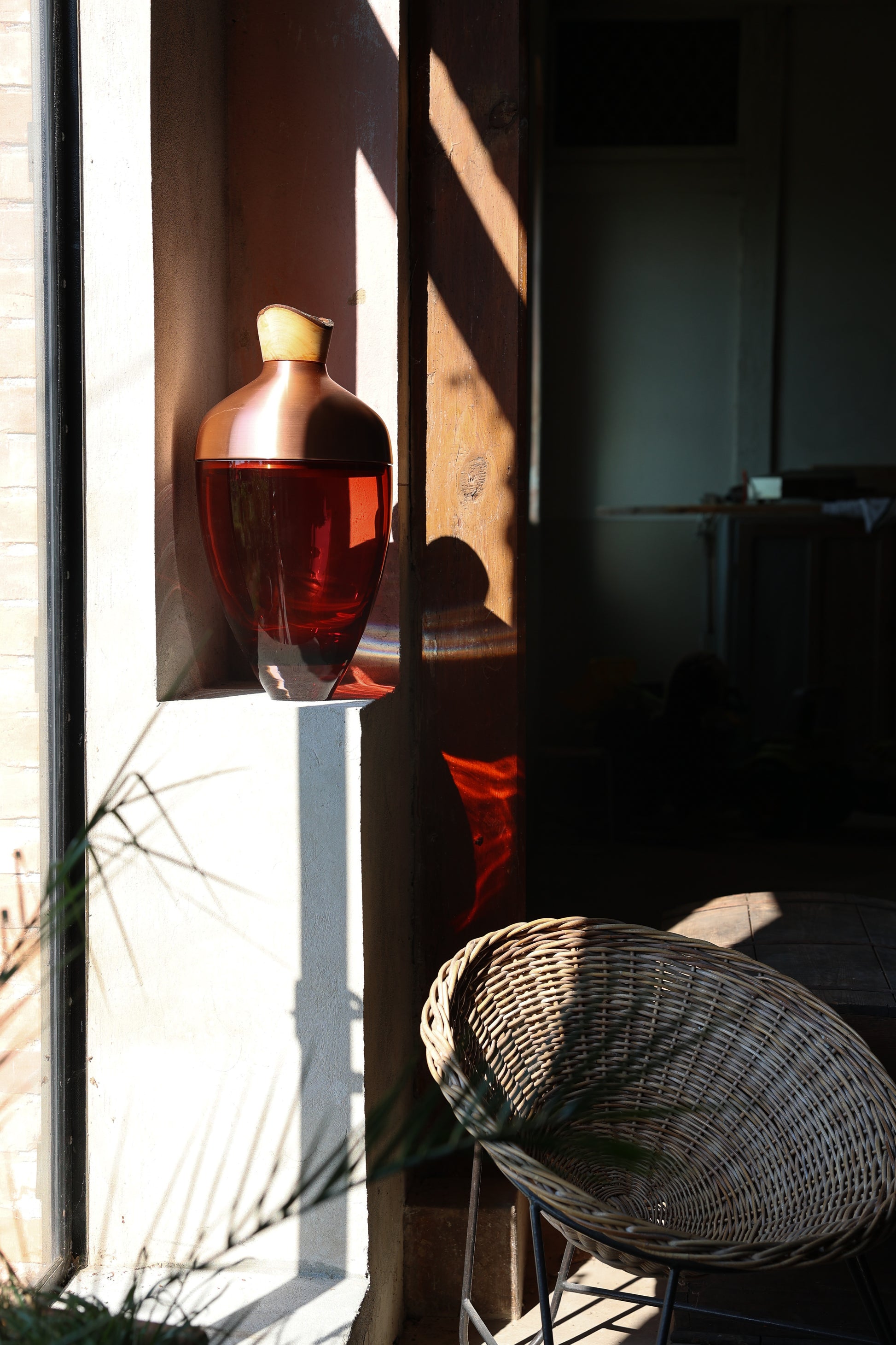 Nani Stacking Vessel in Red & Copper in light, offering a vibrant red color complemented by sleek copper accents, perfect for adding warmth and sophistication to any room.