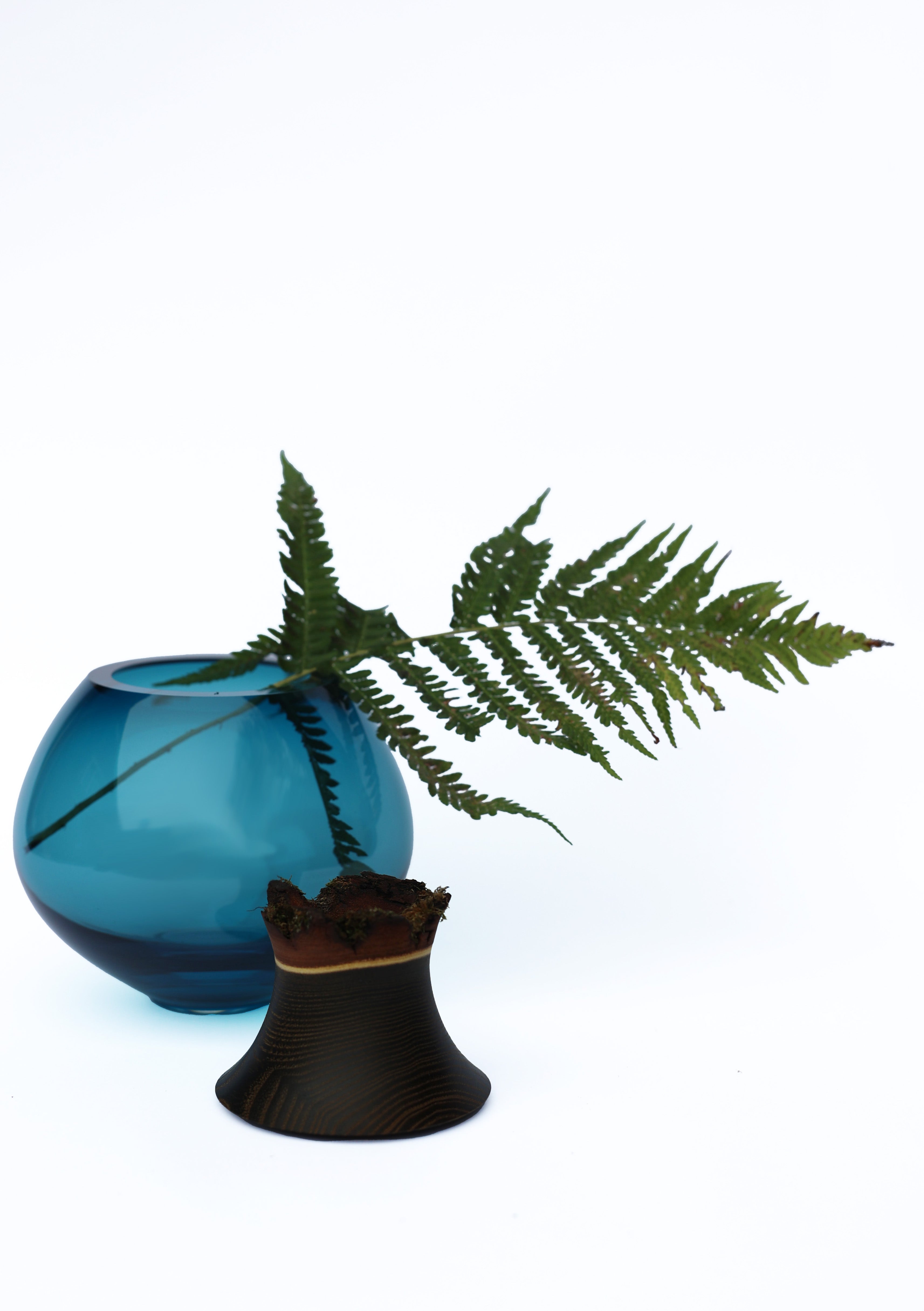 Pisara Stacking Vessel in Blue unstacked with leaf, showcasing an elegant, flowing form with refined craftsmanship.